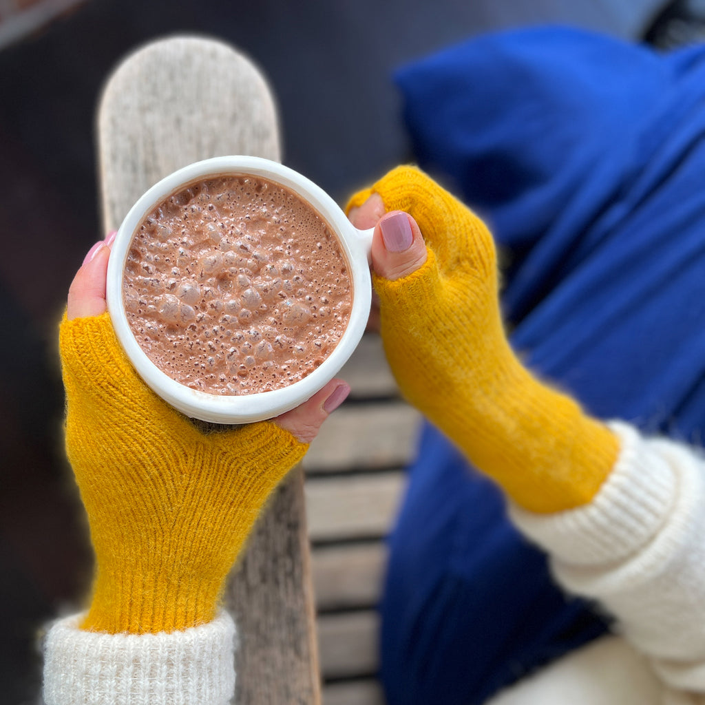 Amy wearing a pair of fingerless gloves in yolk and holding a cup of cacao