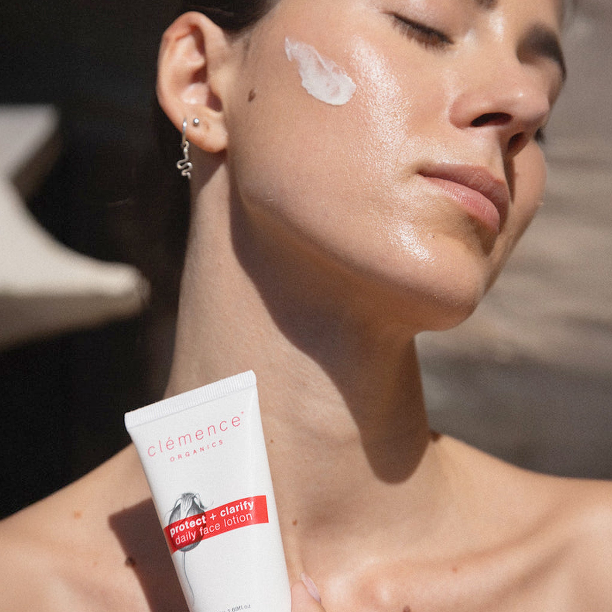 A woman applying Clémence Organics Protect & Clarify Daily Face Lotion SPF 15