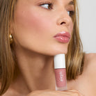 Model wearing and holding a bottle of Aleph Aura Gloss: Bare