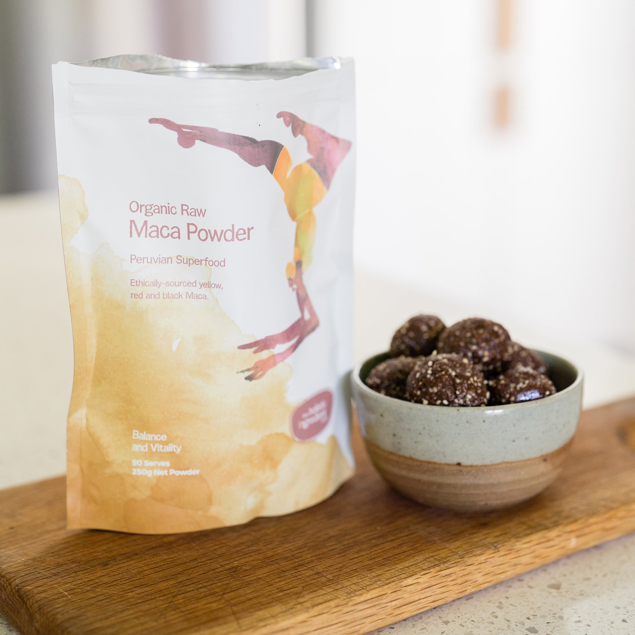 Organic Raw Maca Powder with a bowl of bliss balls on a wooden board.