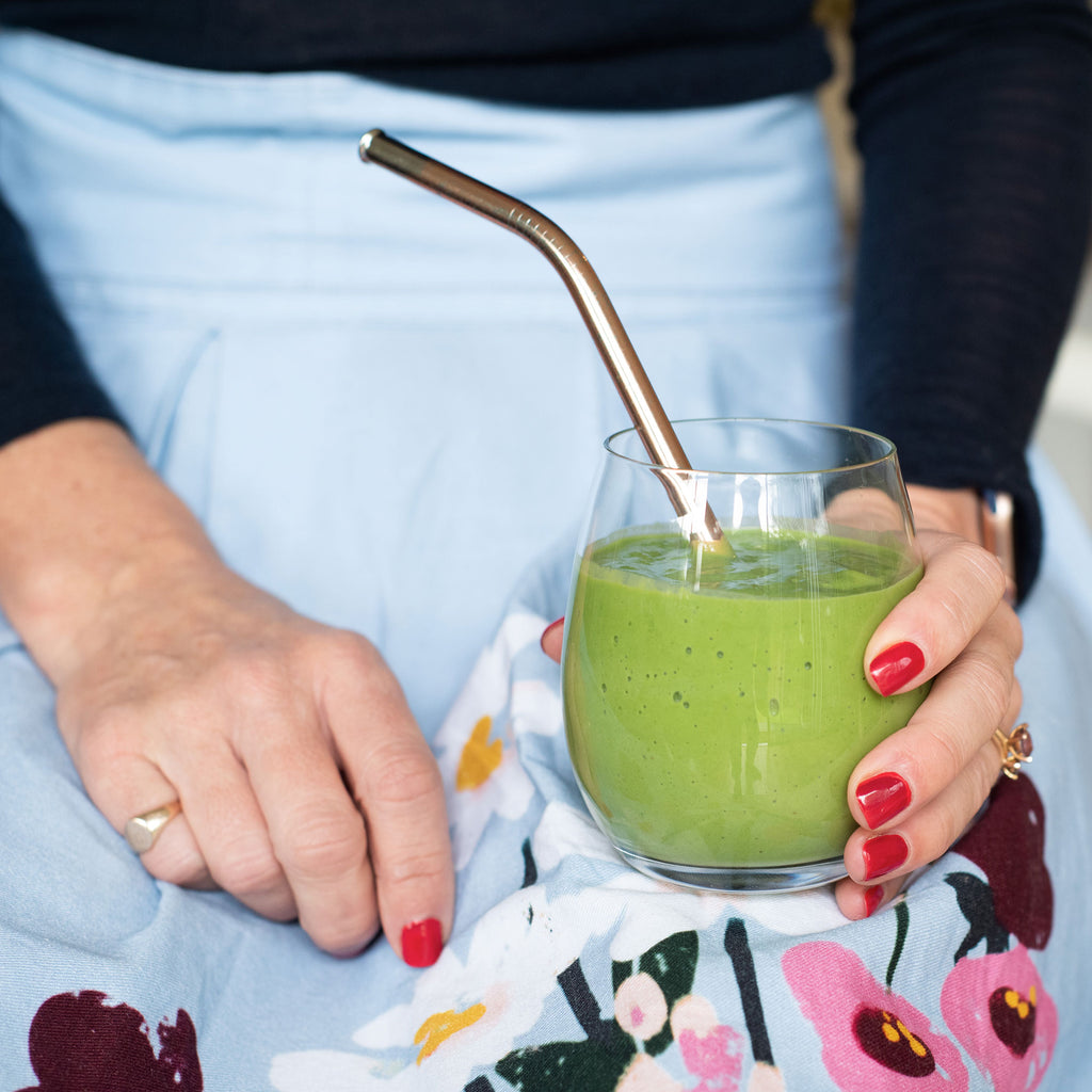 Amy holding a glass of Daily Greens stirred into a smoothie
