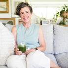 Amy sitting on a couch holding a glass of Daily Greens.