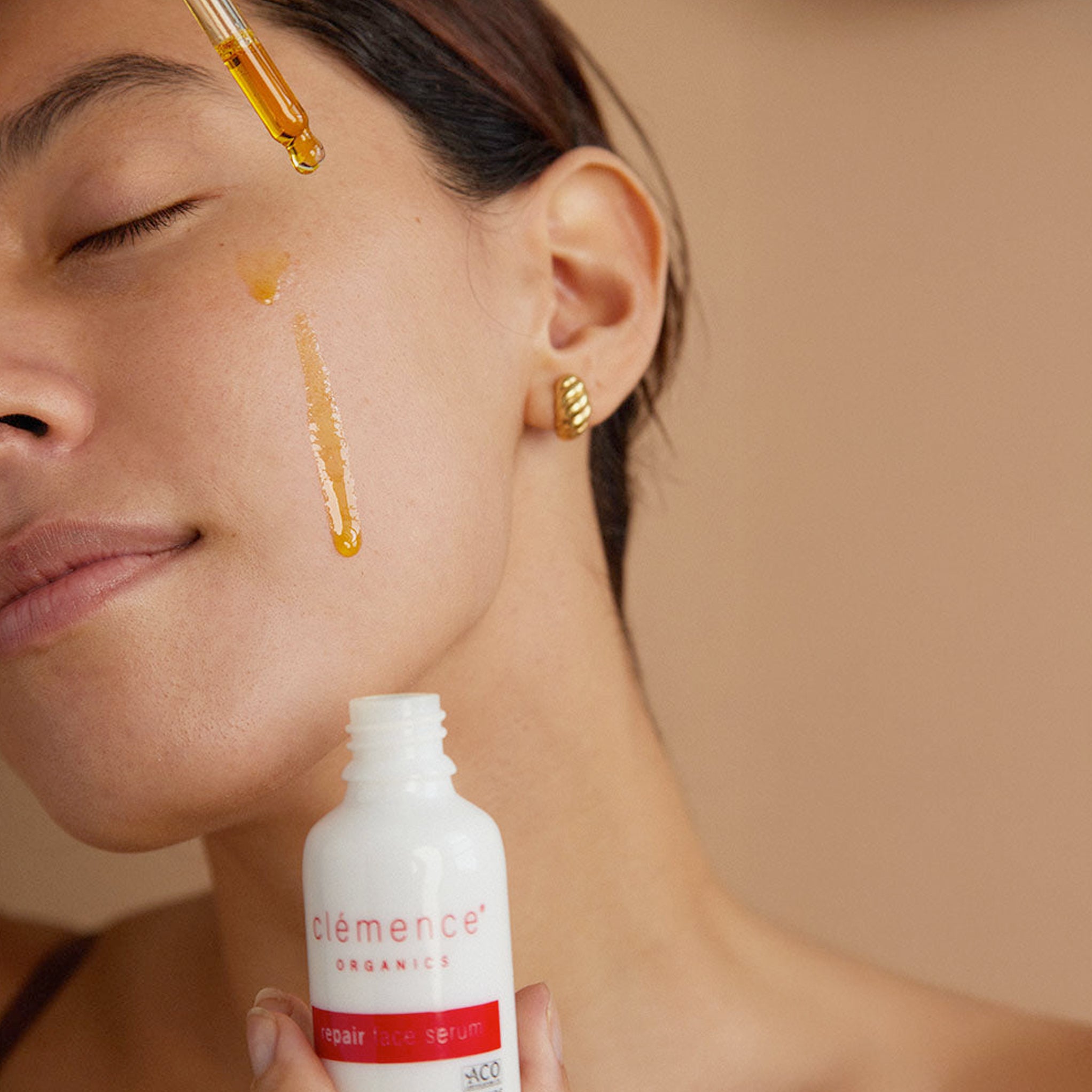 A woman applying Clémence Organics Repair Face Serum to her face
