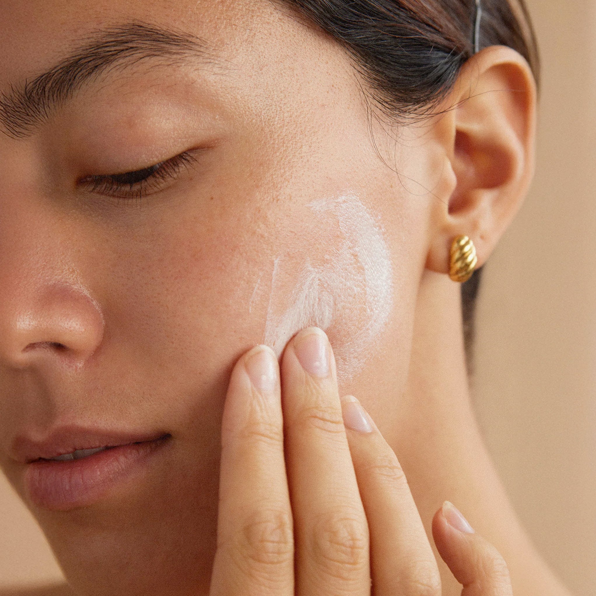 Close-up of a person applying Clémence Organics Ultimate Face Crème to their face with a neutral background