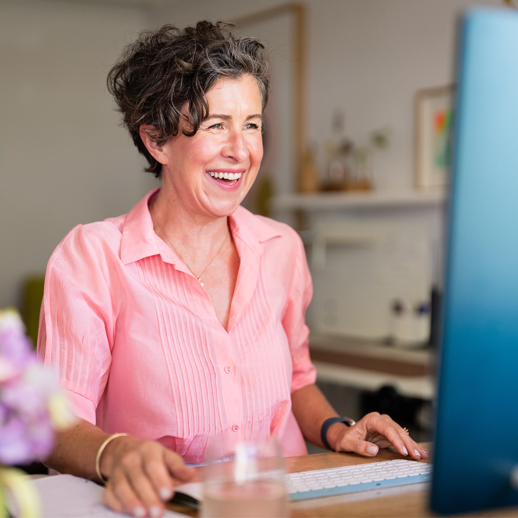 Amy in a pink shirt sitting at a desk with a laptop, smiling.