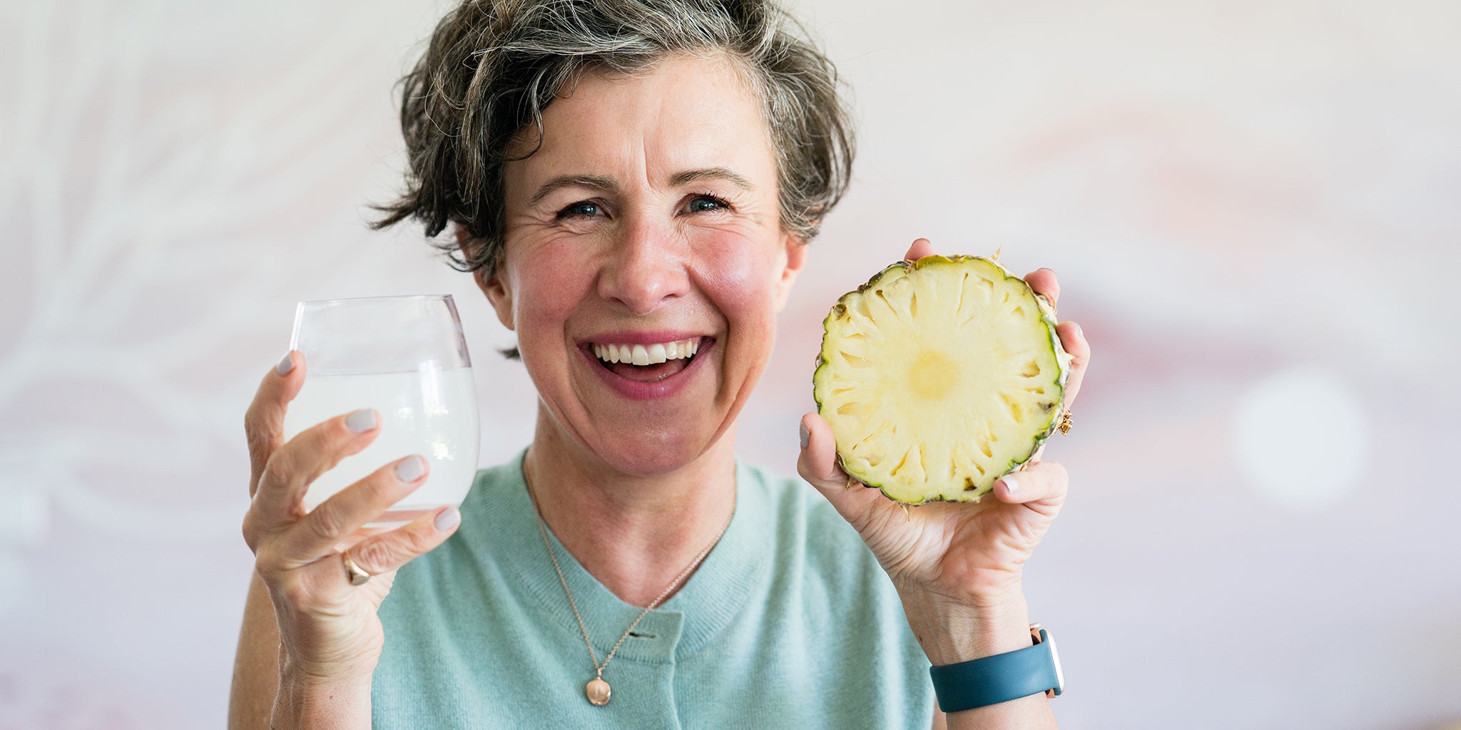 Amy holding a glass of Daily Hydration and a pineapple slice. 