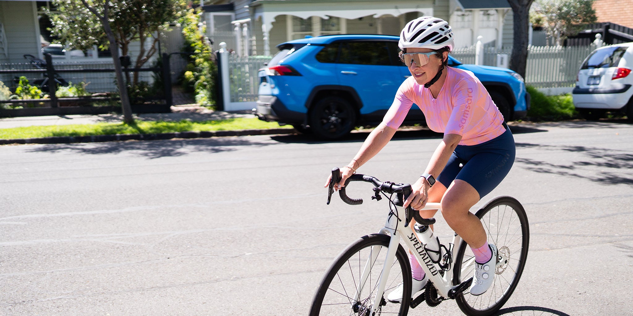 Amy riding a bicycle on a residential street with houses and cars in the background