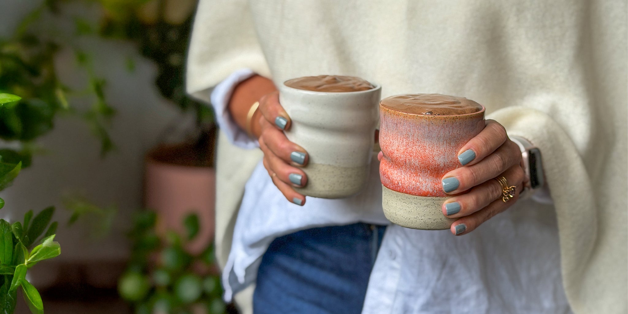 Amy holding two ceramic cups with a blurred indoor background